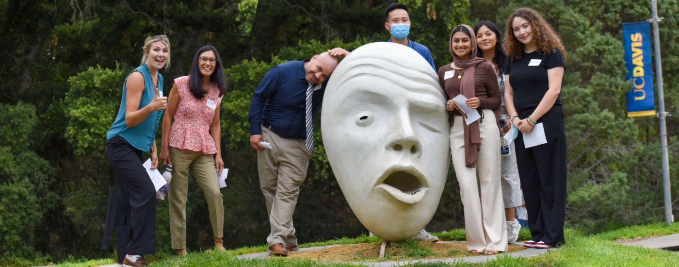 A smiling group of students poses around an egghead sculpture