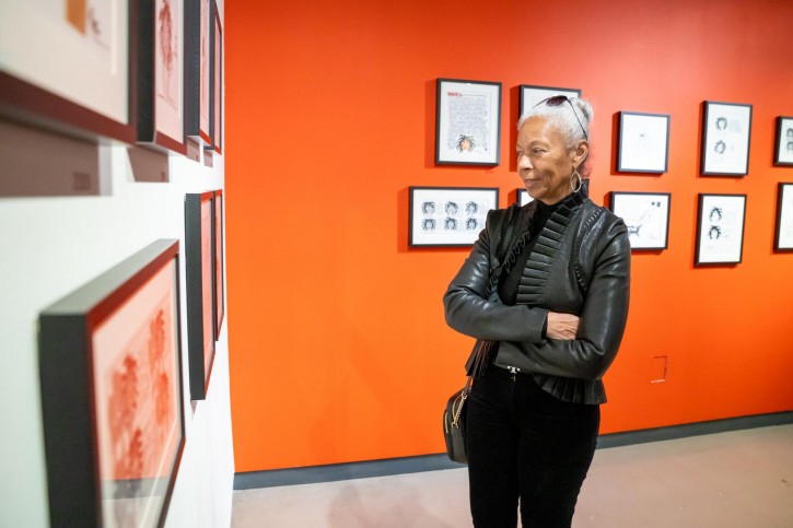 A person in a black leather jacket admires the art in frames along the walls.