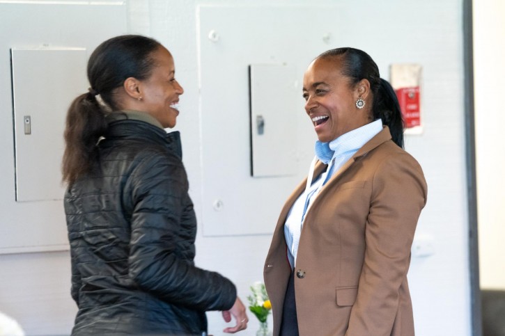 Two woman in ponytails stand together laughing.