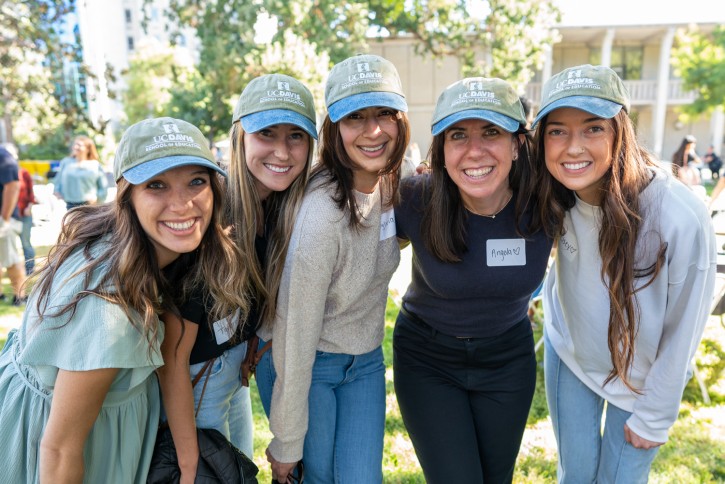 Five women from the College Opportunity Program Educational Talent Search, Shasta wearing green and blue School of Education hats lean together for the photo.