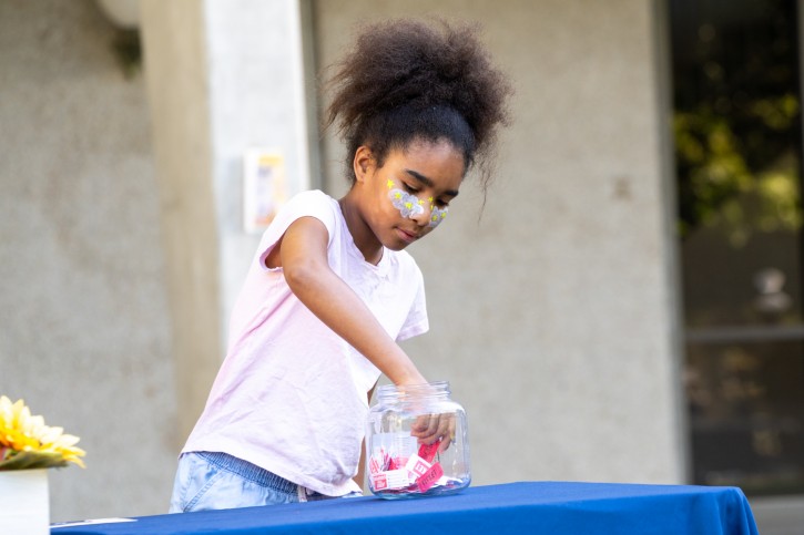 A child with face paint reaches into a jar pulling out a raffle ticket.