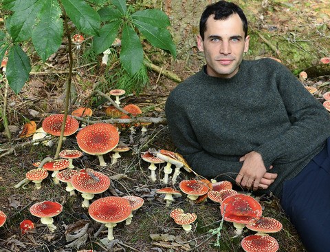 Christian Schwarz in a black turtleneck sitting in a patch of mushrooms