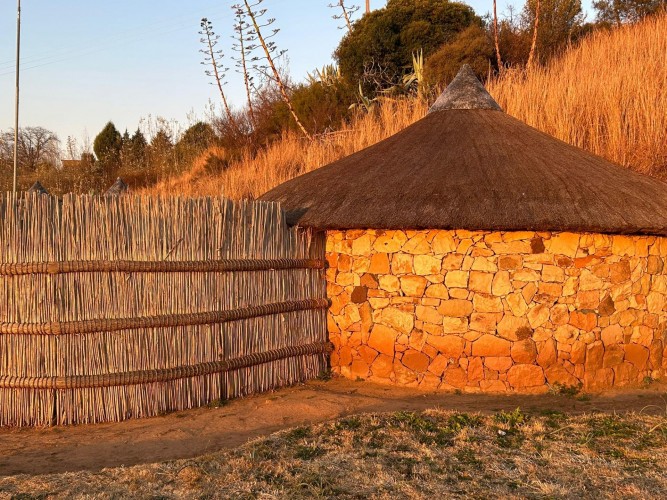 A handmade wooden stick fence next to a round stone building. 