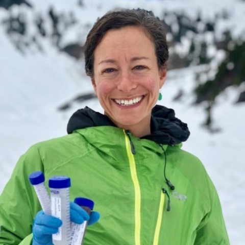 Robin Koder holds up test tubes in front of a snow-covered expanse