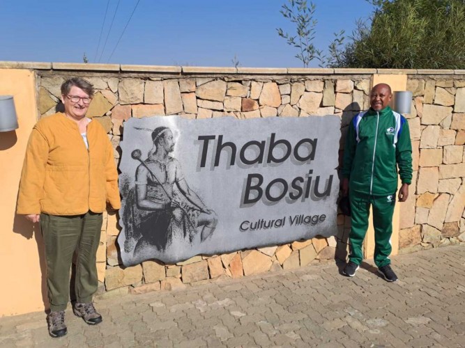 Lauren and Max stand in front of a sign that says "Thaba Bosiu Cultural Village".