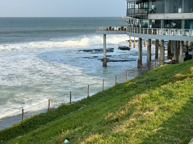 The ocean waves coming in near a building and a grassy area.