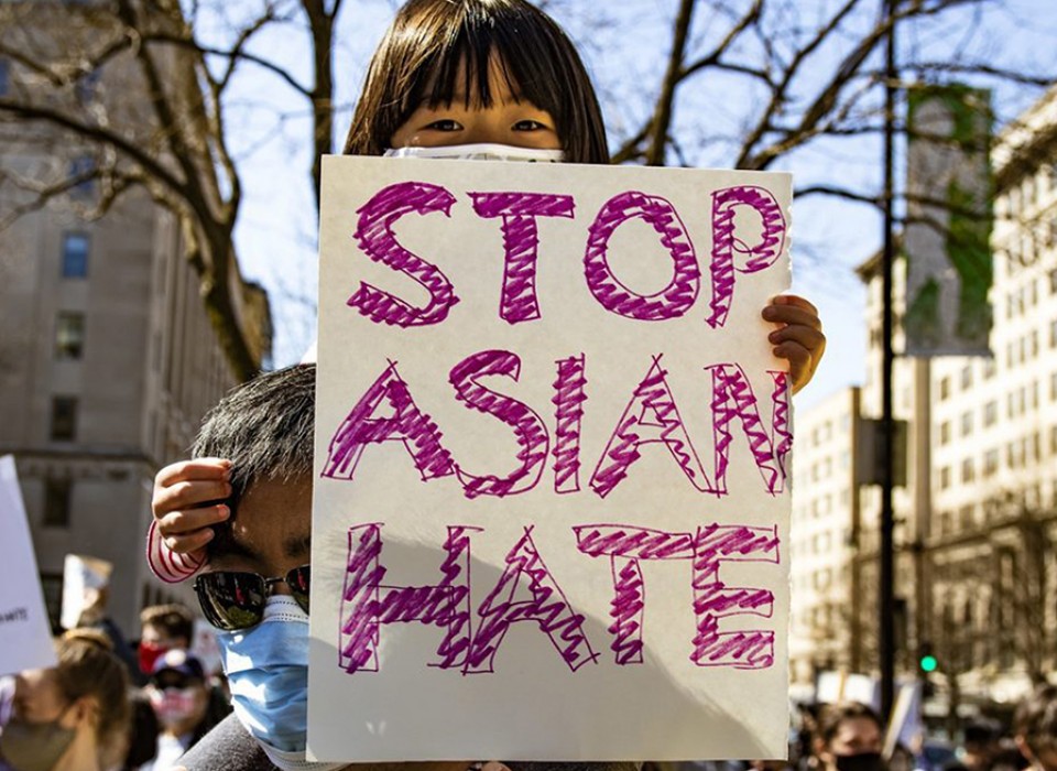 Girl holding up hand-made sign with red letters that spell out "Stop Asian Hate"