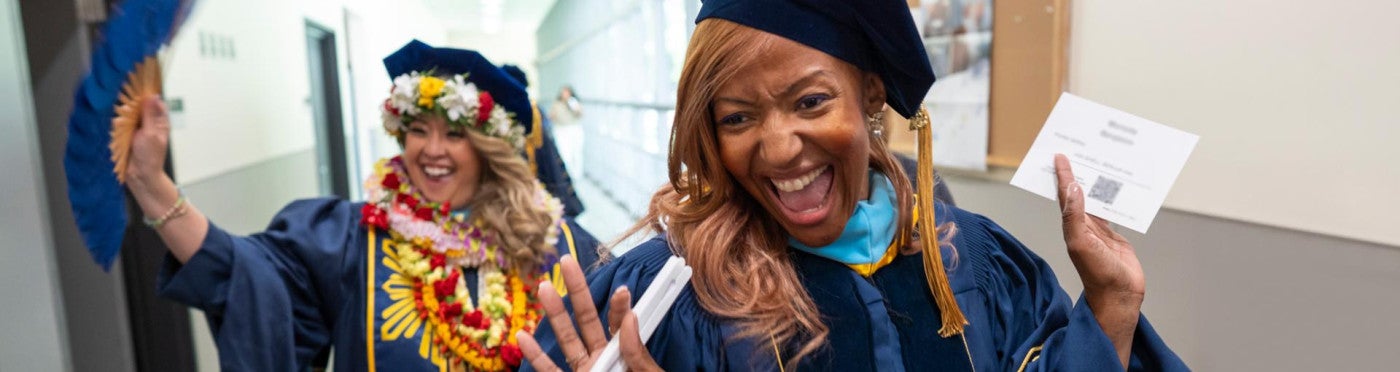 Two graduating Ed.D. students enthusiastically wave at the camera as they process into the ceremony