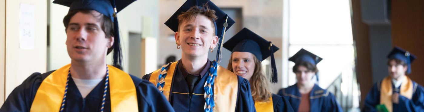 Several Teacher Education students in grad caps and gowns process into Mondavi Center hall