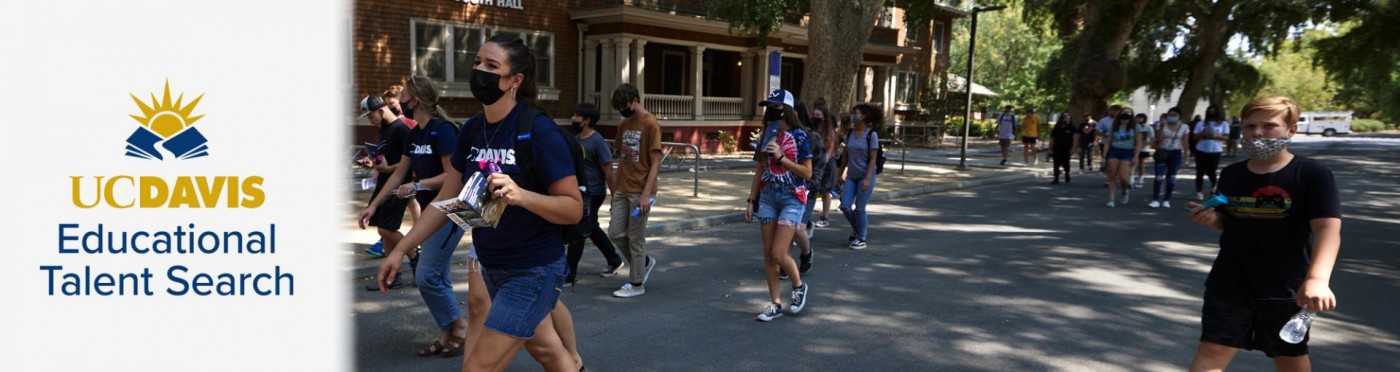 Students in a large dispersed group walk down a road on the UC Davis campus