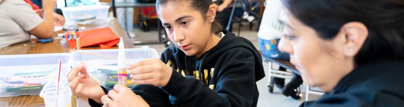 Daughter and mother focusing as they assemble a rocket in a school cafeteria