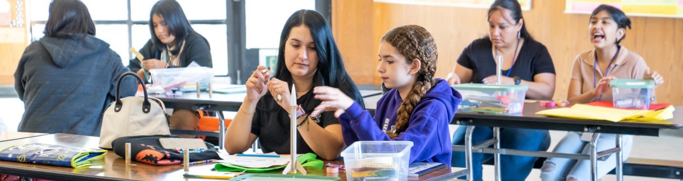 Daughter and mother focusing as they assemble a rocket in a school cafeteria