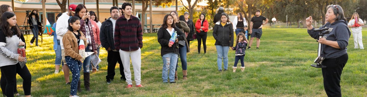 Group of parents and students stand on a lawn outside of a school as Margarita Jimenez-Silva addresses the group