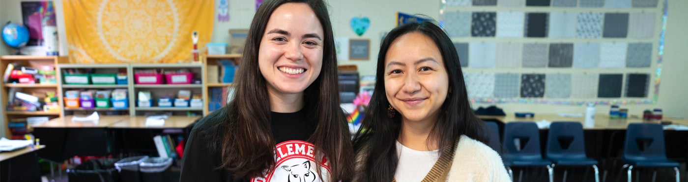 Teaching credential student and mentor teacher stand together smiling in elementary classroom