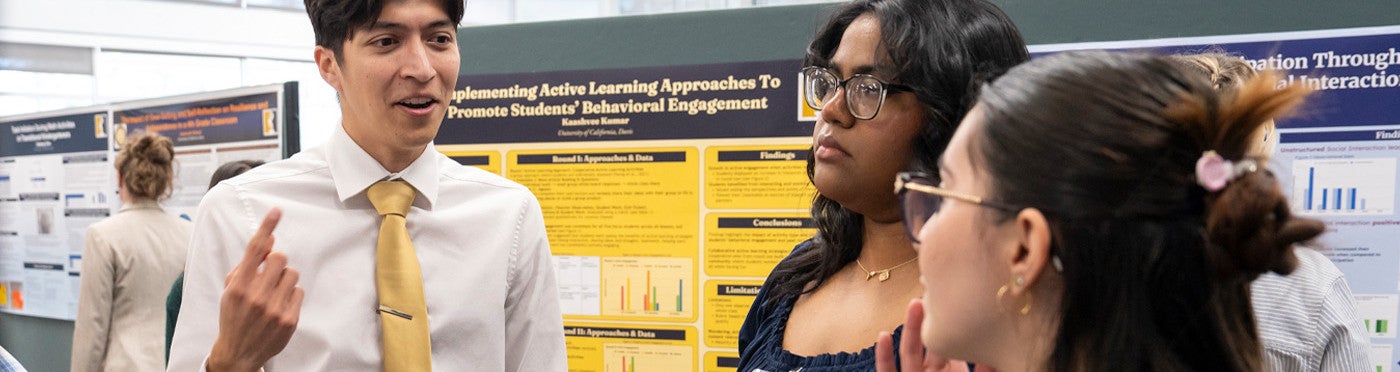 M.A. student explains his research poster to two visitors
