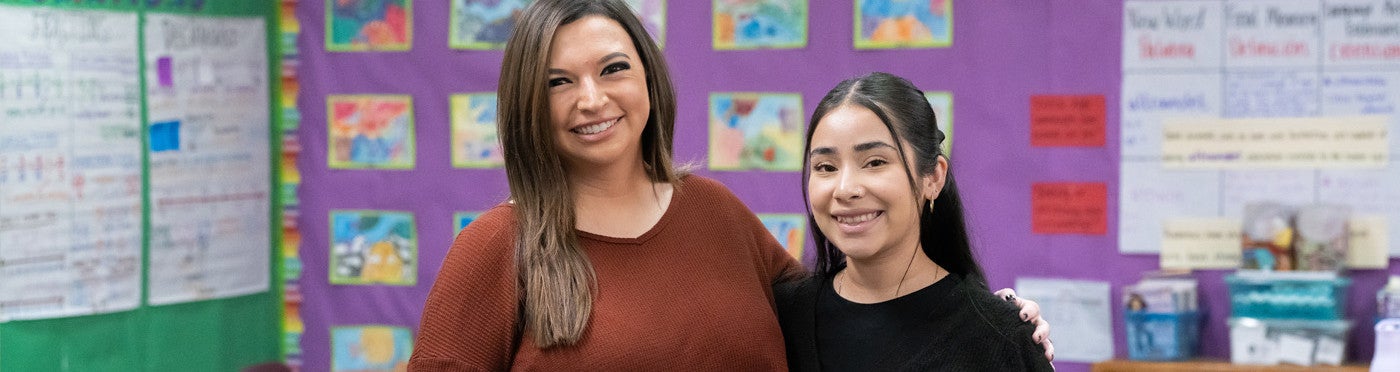 Teaching credential student and mentor teacher stand together smiling in elementary classroom