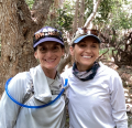 Two women wearing hats and outdoor gear smile and face the camera.