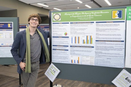 A master's candidate stands next to his research poster titled "Meaning in the Margins: The Impact of Scaffolded Annotation on Comprehension in the 6th Grade Classroom."