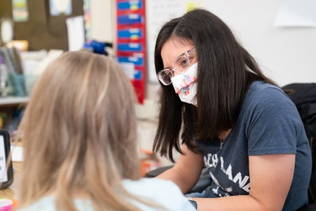 An elementary school teacher wearing a mask providing instructor to a student