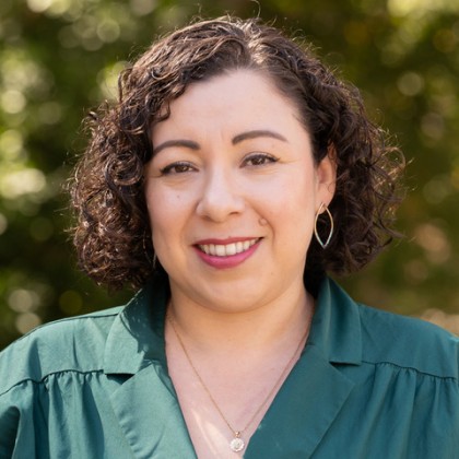 Dr. Claudia Rodriguez-Mojica poses for a headshot in front of trees while wearing a green shirt.