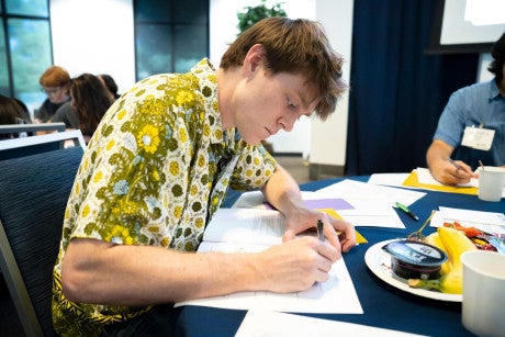 A credential student wearing a green button-up shirt writes in his program handbook.