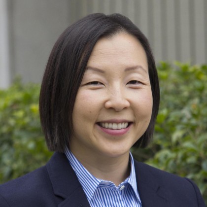 Headshot of Jennifer Higgs wearing a suit and standing in front of topiary