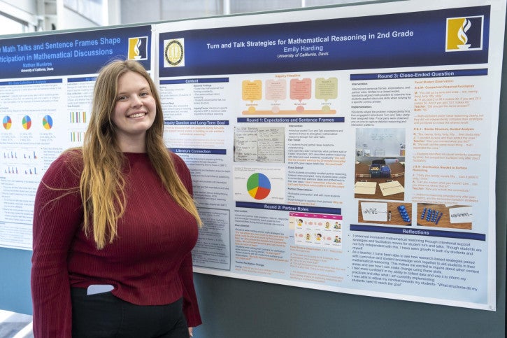 A woman in a red sweater stands smiling in front of a detailed academic poster about elementary mathematical reasoning strategies.