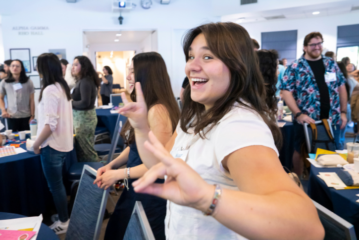A student smiles at the camera, holding up "quiet coyote" hand symbols