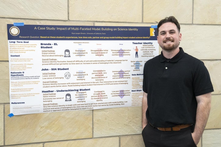 Man in black polo stands smiling beside a poster titled "A Case Study: Impact of Multi-Faceted Model Building on Science Identity." The poster is filled with text and graphics related to student experiences and model building in science education. 