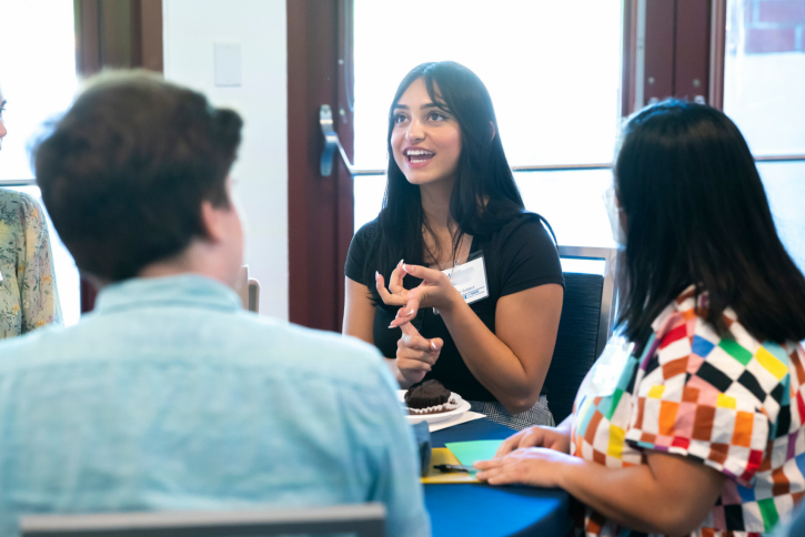 A student smiles and speaks to others at her table.