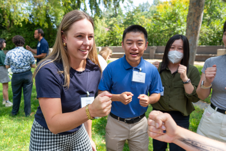 Two students play rock paper scissors while others cheer them on.