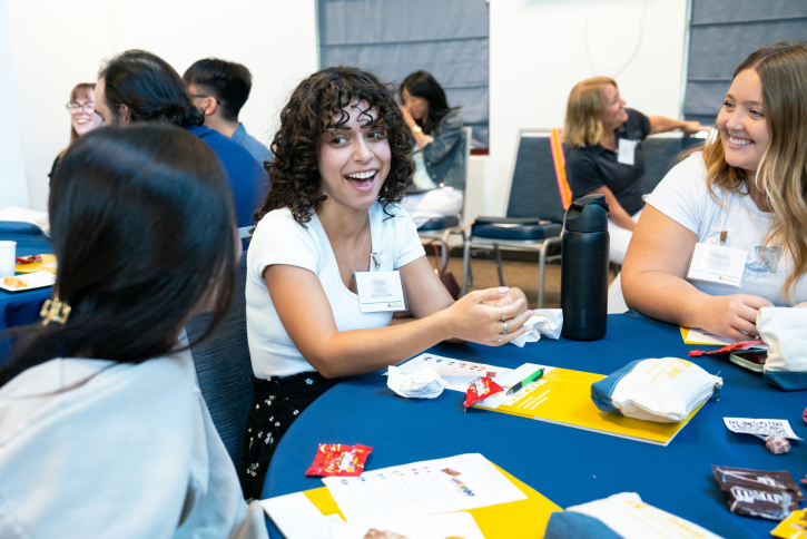 Three students smile and talk around a table.