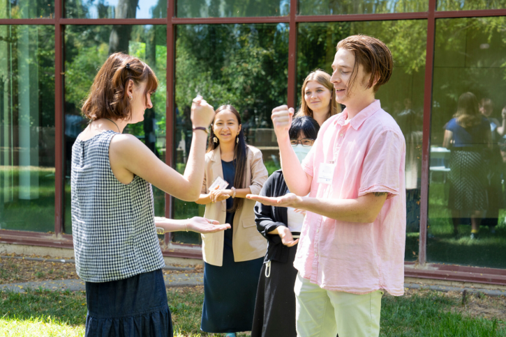 Two students play rock paper scissors. Behind them, a couple of their classmates smile and watch.