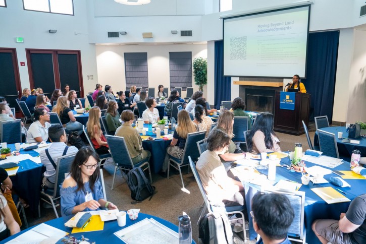 Students, staff, and faculty sit at round tables.