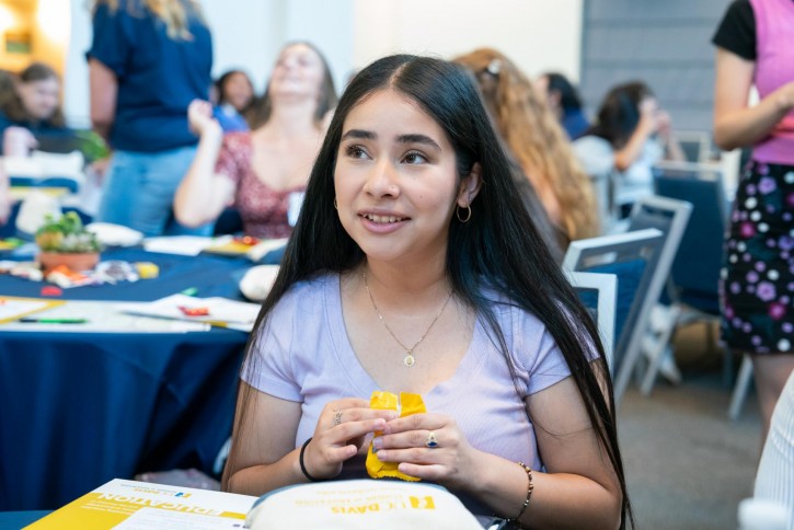 A student in a purple shirt with long black hair smiles.