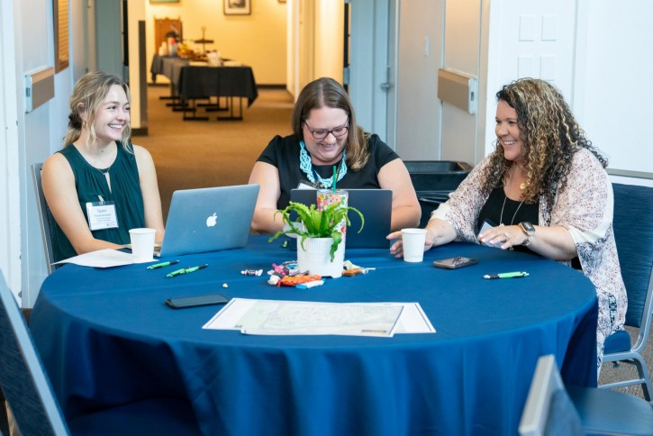 Three faculty members smile and laugh.