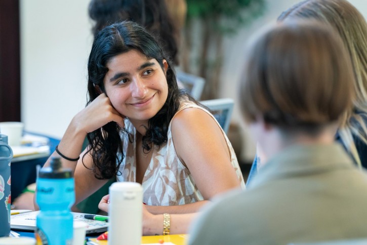 A girl with dark hair listens to the person next to her speaking.