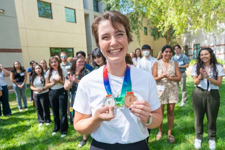 A student with short hair smiles widely as she holds up her silver and bronze medals.