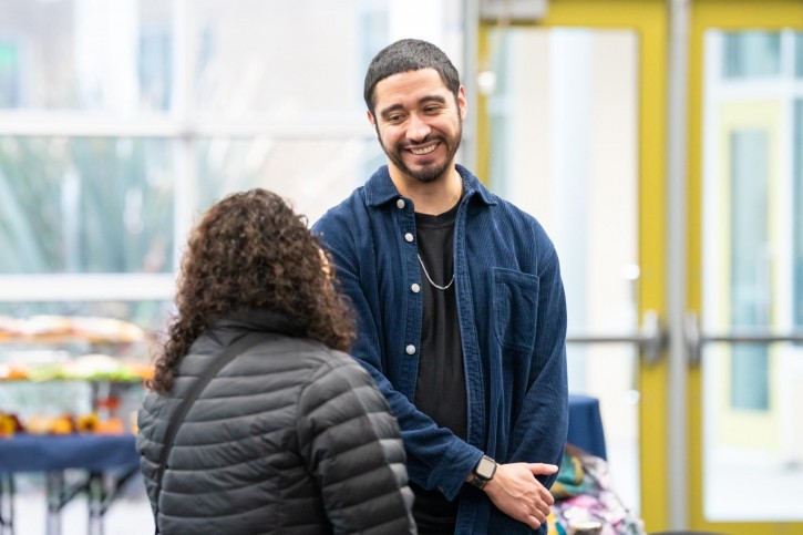 A man wearing a blue button down smiles at a woman who is facing away from the camera.