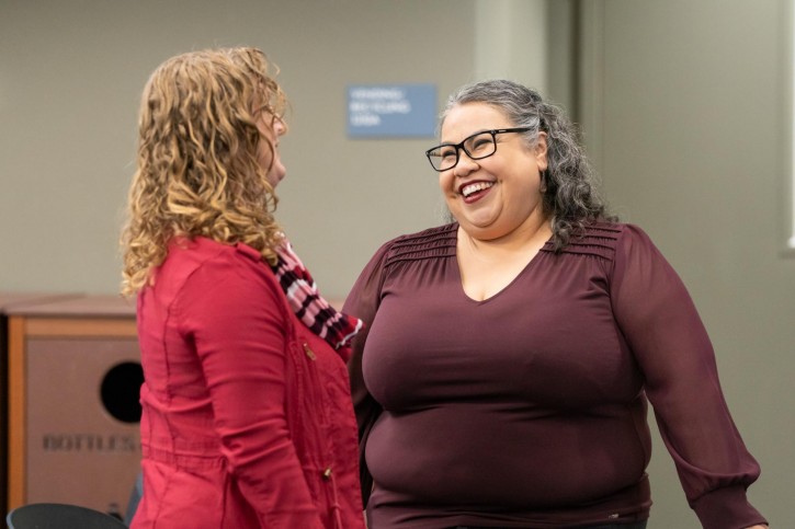 Marcela Cuellar smiles at a woman wearing red who faces away from the camera.