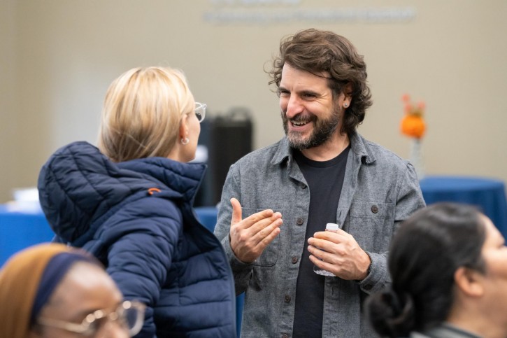 A man gestures with his hands to a woman wearing a down coat who faces away from the camera.