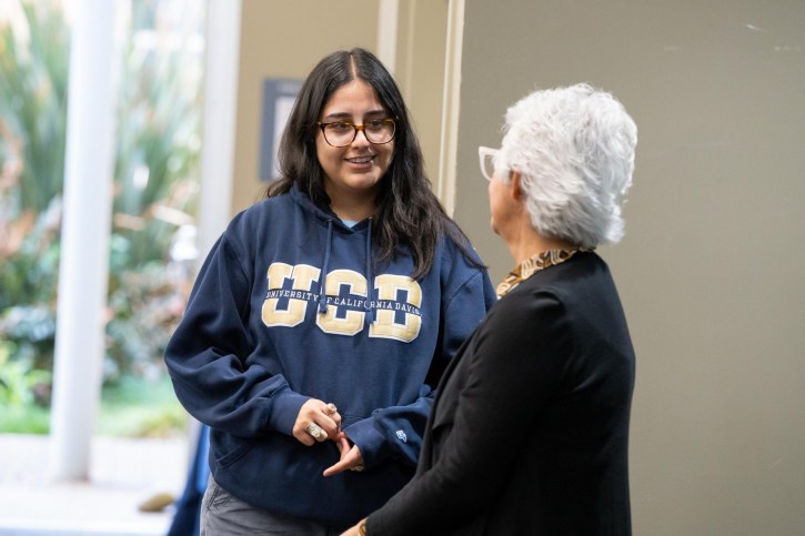 A woman wearing a navy UC Davis sweatshirt speaks to a second woman who faces away from the camera.