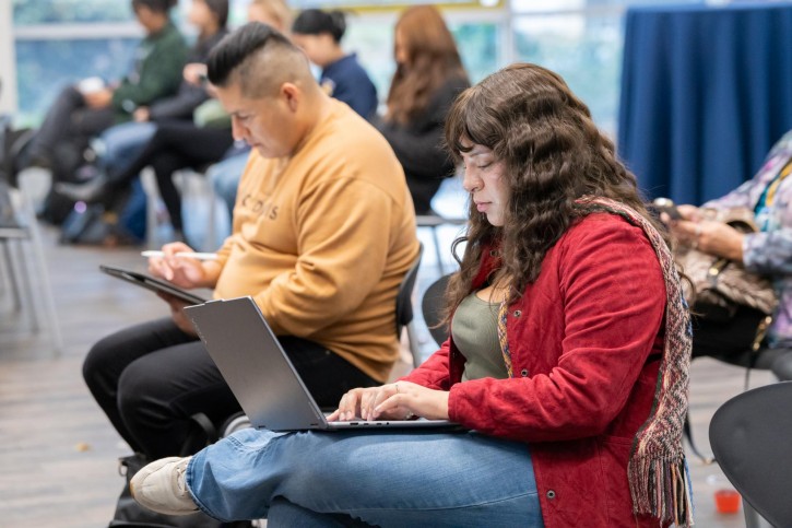 Two people sit in the audience, typing on their computers.