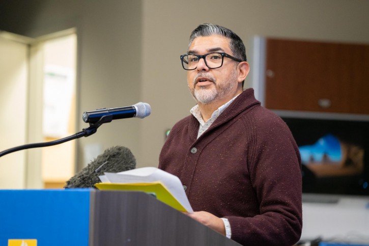 Danny C. Martinez stands at the podium, faces the audience, and speaks into a microphone.