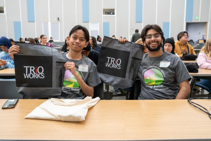 Two teenagers pose with bags that say "TRIO WORKS."