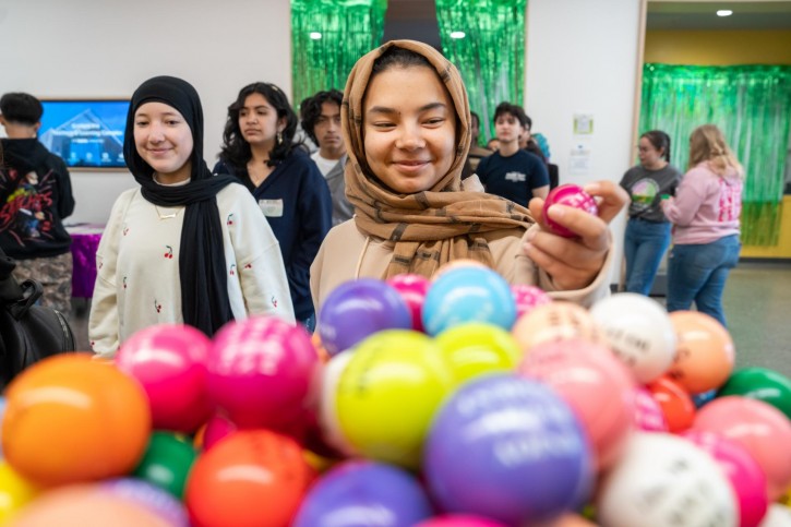 A girl wearing a hijab looks at a bowl of gumballs.