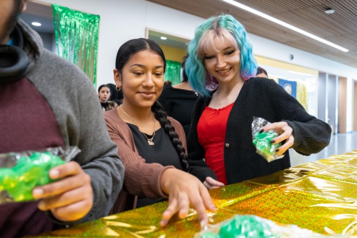 Two girls look down at a table covered with branded merchandise and a shiny yellow tablecloth.