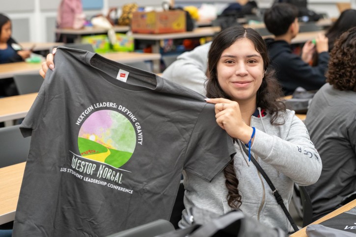 A girl holds up an event t-shirt that says "WESTOP NORCAL."