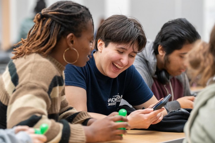 Two students look down at a phone they're holding, both laughing.