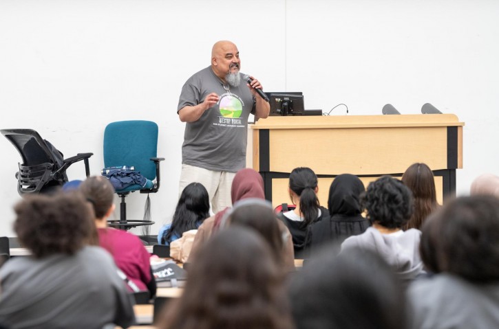 Samuel Blanco III stands at a podium, addressing an audience sitting in front of him.